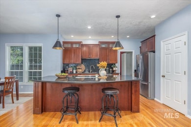 Kitchen with stainless steel refrigerator with ice dispenser, dark countertops, light wood-type flooring, backsplash, and recessed lighting