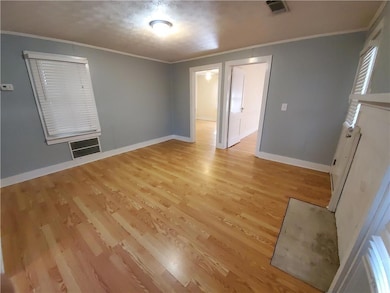 Empty room with light wood-style flooring, baseboards, and crown molding
