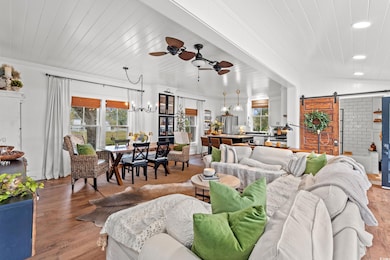 Living area featuring a barn door, a ceiling fan, light wood-type flooring, a chandelier, and recessed lighting
