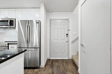 Kitchen featuring tasteful backsplash, dark stone countertops, dark hardwood / wood-style flooring, white cabinets, and appliances with stainless steel finishes