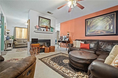 Living area with carpet, ceiling fan, a fireplace, and a textured ceiling