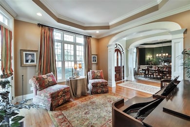 Sitting room with arched walkways, a tray ceiling, wood finished floors, and ornate columns