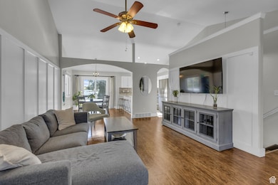 Living area with dark wood finished floors, arched walkways, ceiling fan, a chandelier, and vaulted ceiling