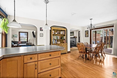 Kitchen with arched walkways, light wood-type flooring, a fireplace, a chandelier, and hanging light fixtures