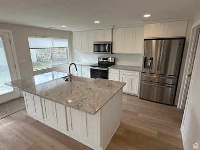 Kitchen featuring appliances with stainless steel finishes, white cabinetry, light stone countertops, light wood finished floors, and recessed lighting