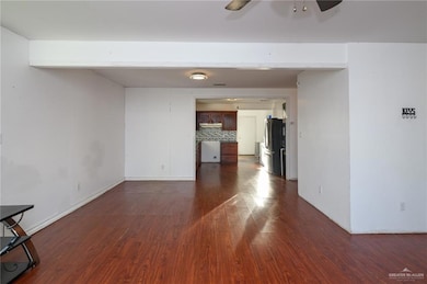Empty room featuring dark wood-style flooring, ceiling fan, and baseboards
