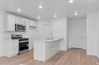 Kitchen with appliances with stainless steel finishes, light wood-style floors, recessed lighting, white cabinets, and a peninsula