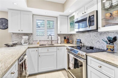 Kitchen featuring light tile patterned flooring, white cabinets, appliances with stainless steel finishes, a sink, and light stone counters