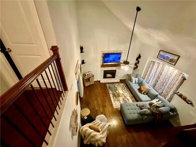 Living area featuring a stone fireplace, stairs, vaulted ceiling, and wood finished floors