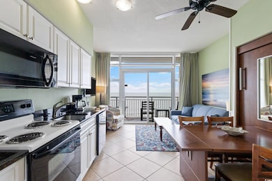 Kitchen featuring range with electric stovetop, a textured ceiling, black microwave, a wall of windows, and white cabinetry