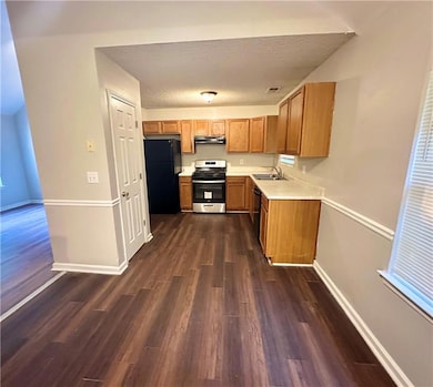 Kitchen with black appliances, under cabinet range hood, light countertops, dark wood-style floors, and baseboards