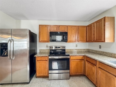 Kitchen with appliances with stainless steel finishes, a textured ceiling, light stone countertops, brown cabinetry, and light tile patterned floors
