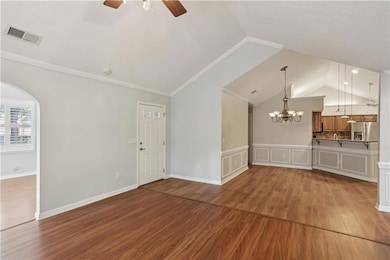 Unfurnished living room featuring wood finished floors, vaulted ceiling, a ceiling fan, crown molding, and arched walkways