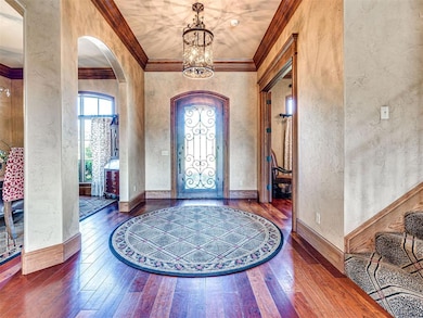 Foyer entrance featuring a textured wall, wood-type flooring, a chandelier, arched walkways, and ornamental molding