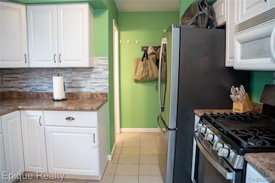 Kitchen with white cabinetry, stainless steel appliances, light tile patterned flooring, and backsplash