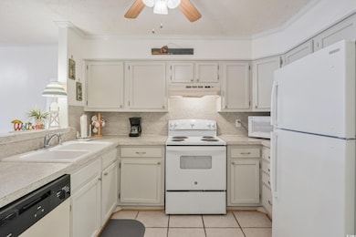 Kitchen featuring white appliances, light countertops, under cabinet range hood, a sink, and light tile patterned flooring