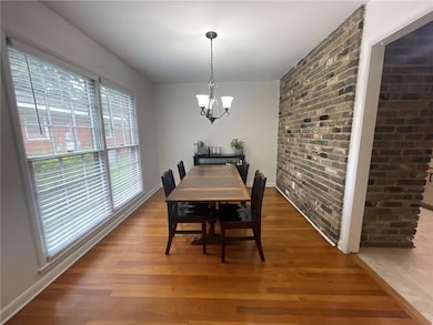 Dining area with a chandelier, wood finished floors, brick wall, and baseboards