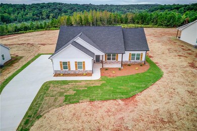 View of front of home with a wooded view, stone siding, a shingled roof, driveway, and covered porch