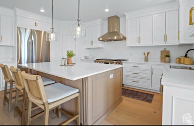 Kitchen with a center island, wall chimney range hood, a kitchen bar, and white cabinetry