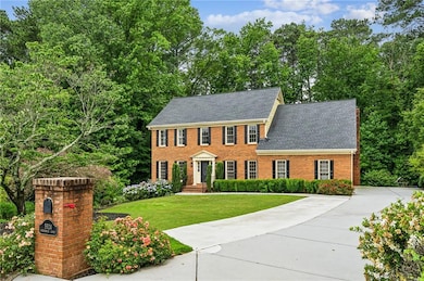 Colonial inspired home with brick siding, a front yard, roof with shingles, and view of wooded area