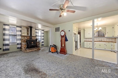 Living room featuring a wood stove, a ceiling fan, a chandelier, and light carpet