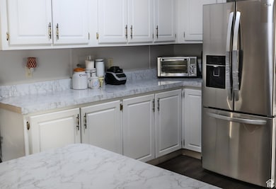 Kitchen with stainless steel refrigerator with ice dispenser, white cabinets, dark wood-style floors, and light stone counters