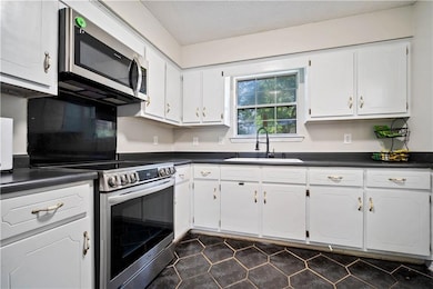 Kitchen with stainless steel appliances, dark countertops, white cabinetry, and a textured ceiling