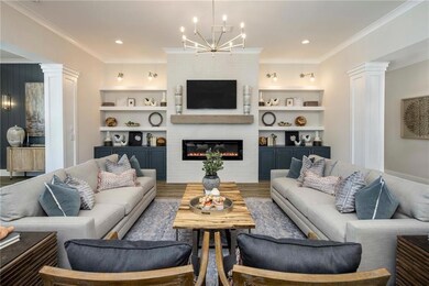 Living room with ornate columns, ornamental molding, a chandelier, a large fireplace, and wood finished floors