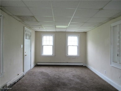 Carpeted empty room with a baseboard heating unit and a drop ceiling