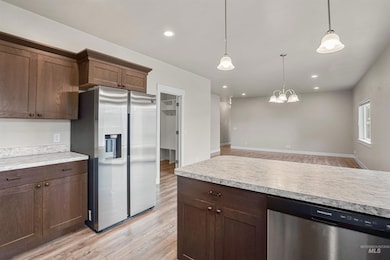 Kitchen with stainless steel appliances, light wood-type flooring, light countertops, dark brown cabinetry, and decorative light fixtures