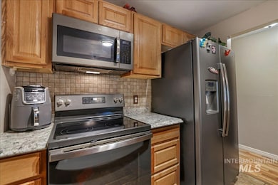 Kitchen with appliances with stainless steel finishes, backsplash, light stone counters, and light wood-style flooring