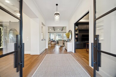 Step into an impressive foyer where modern elegance meets timeless design. The striking steel and glass front doors create a grand entrance, flooding the space with natural light while offering a sleek, contemporary touch. This inviting entryway sets the tone for the rest of the home, combining sophistication with an open, airy ambiance.