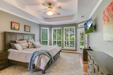 Bedroom featuring a raised ceiling, wood finished floors, access to exterior, ceiling fan, and ornamental molding