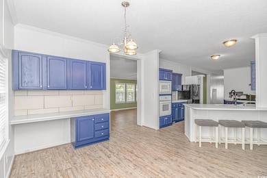 Kitchen featuring white appliances, blue cabinetry, a kitchen bar, a sink, and a peninsula