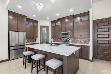 Kitchen featuring glass insert cabinets, stainless steel appliances, light stone countertops, light tile patterned floors, and a breakfast bar