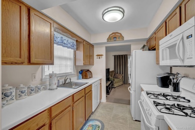 Kitchen featuring white appliances, light countertops, light tile patterned floors, and brown cabinets