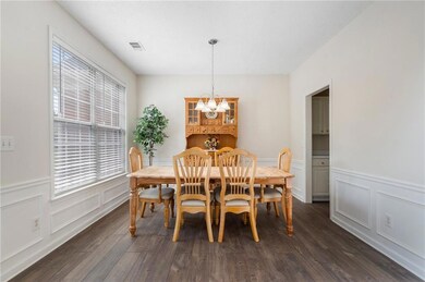 Dining area featuring a chandelier, a decorative wall, wainscoting, and dark wood-type flooring