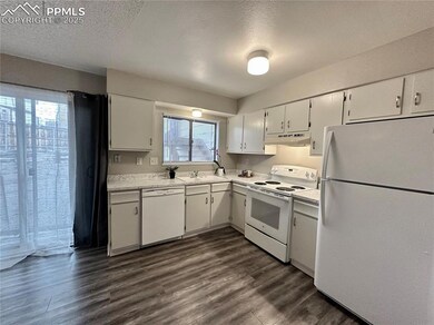 Kitchen featuring white appliances, under cabinet range hood, a textured ceiling, dark wood-style flooring, and light countertops