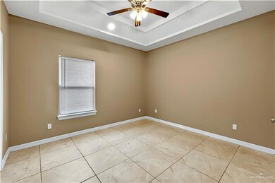 Empty room featuring a raised ceiling, a ceiling fan, and light tile patterned floors