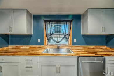 Kitchen with stainless steel dishwasher, butcher block counters, and white cabinets, farm house sink