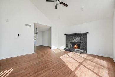 Unfurnished living room with visible vents, a ceiling fan, wood finished floors, a stone fireplace, and baseboards
