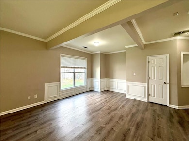 Unfurnished room featuring dark wood-type flooring, crown molding, and a wainscoted wall
