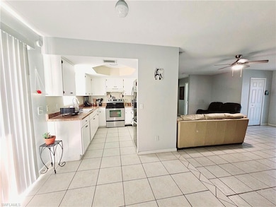 Kitchen with stainless steel appliances, light tile patterned floors, a sink, white cabinetry, and ceiling fan