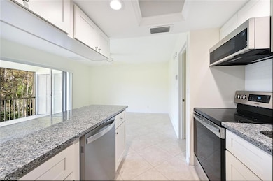 Kitchen with appliances with stainless steel finishes, light stone counters, white cabinets, and a tray ceiling
