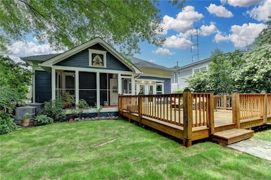 Back of property featuring a sunroom, a lawn, a wooden deck, and cooling unit