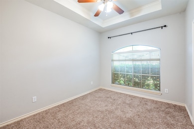 Carpeted empty room with a raised ceiling, ornamental molding, and ceiling fan