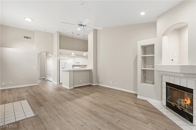 Unfurnished living room featuring arched walkways, a tile fireplace, light wood-style floors, a high ceiling, and a ceiling fan