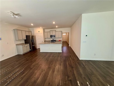 Kitchen featuring stainless steel appliances, dark wood-style flooring, a center island with sink, light stone counters, and recessed lighting