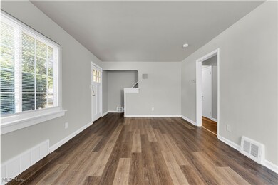 Unfurnished living room featuring dark wood-style flooring and baseboards
