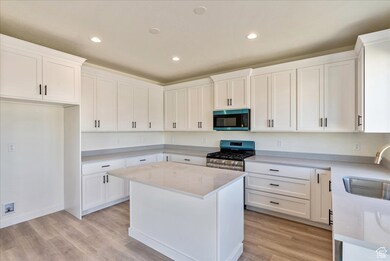 Kitchen featuring white cabinets, light wood-type flooring, stainless steel appliances, a kitchen island, and recessed lighting